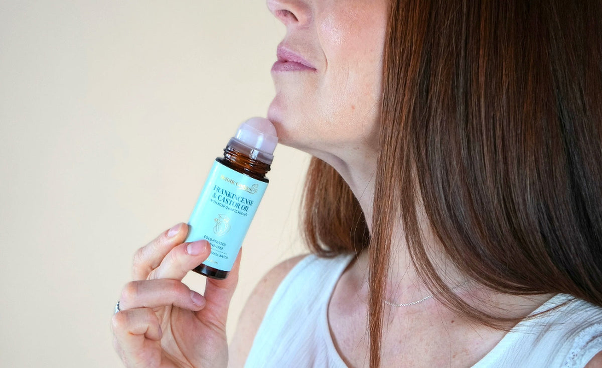 Woman applying Holistic Goddess Frankincense Castor Oil roll-on along her jawline as part of her morning skincare routine