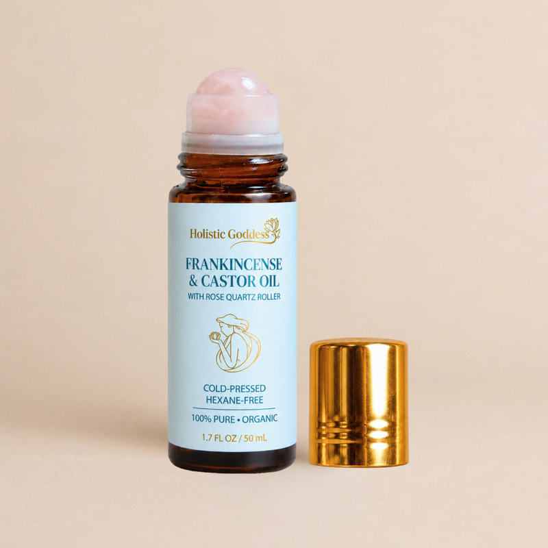 Holistic Goddess Frankincense & Castor Oil in an amber glass roller bottle with a pink rose quartz roller ball and a separate gold cap, set against a solid beige background.