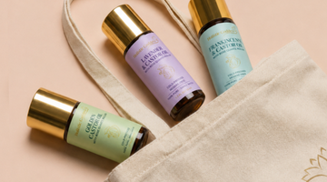 Three castor oil rollers arranged on a beige canvas tote bag against a soft peach background. 