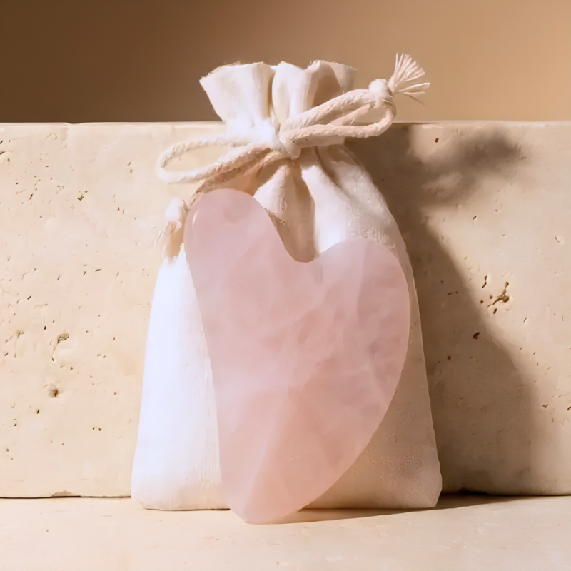 Gua Sha Stone by BeWell – rose quartz gua sha stone leaning against its drawstring pouch on stone surface