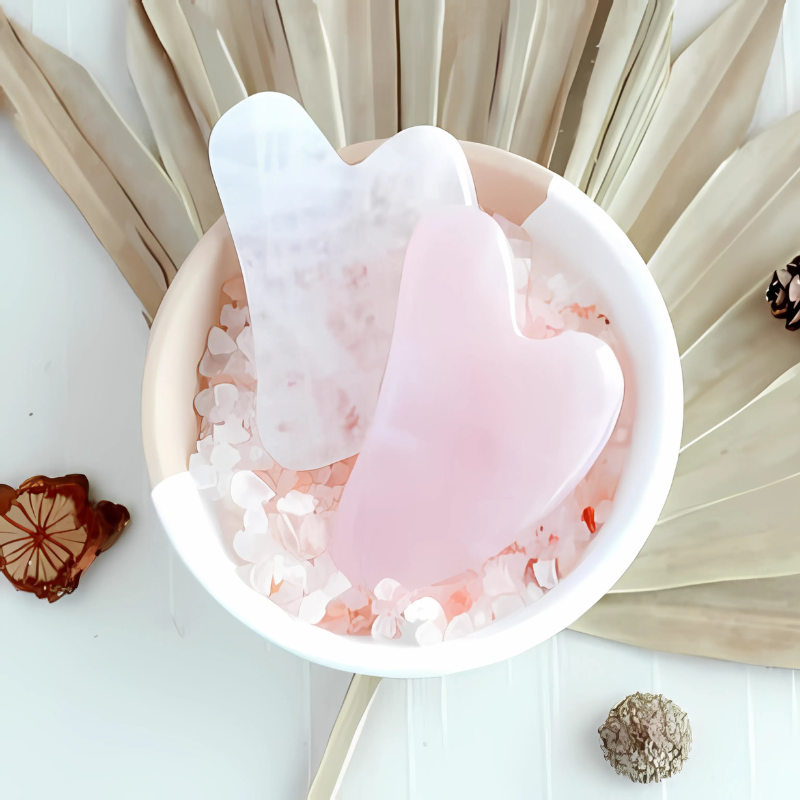 Gua Sha Stone – two gua sha stones (clear + rose quartz) in a bowl of pink and clear crystal chips, styled flat-lay with d...