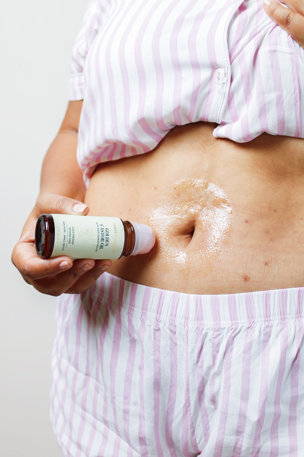 Woman applying Golden Castor Oil roll-on to her abdomen for body skincare
