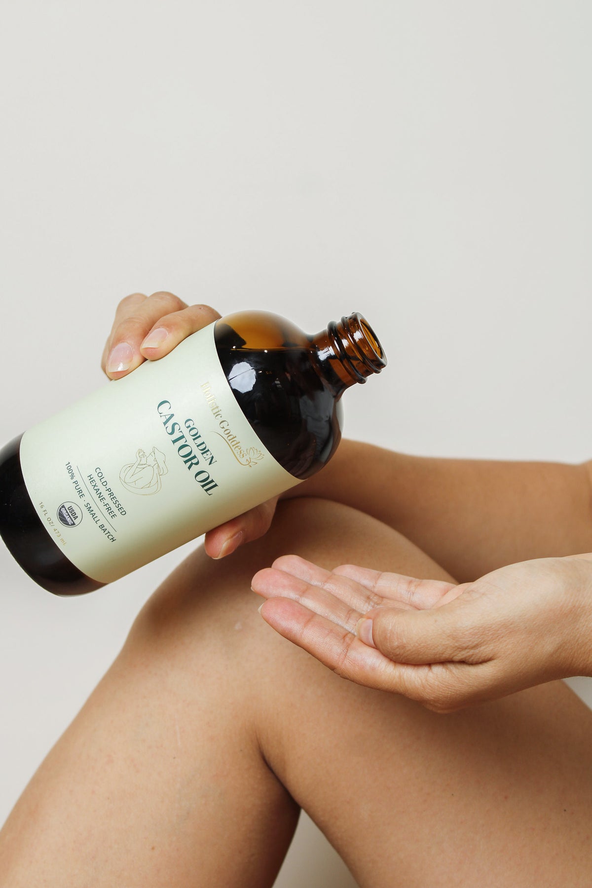 Woman applying Holistic Goddess Golden Castor Oil to her skin