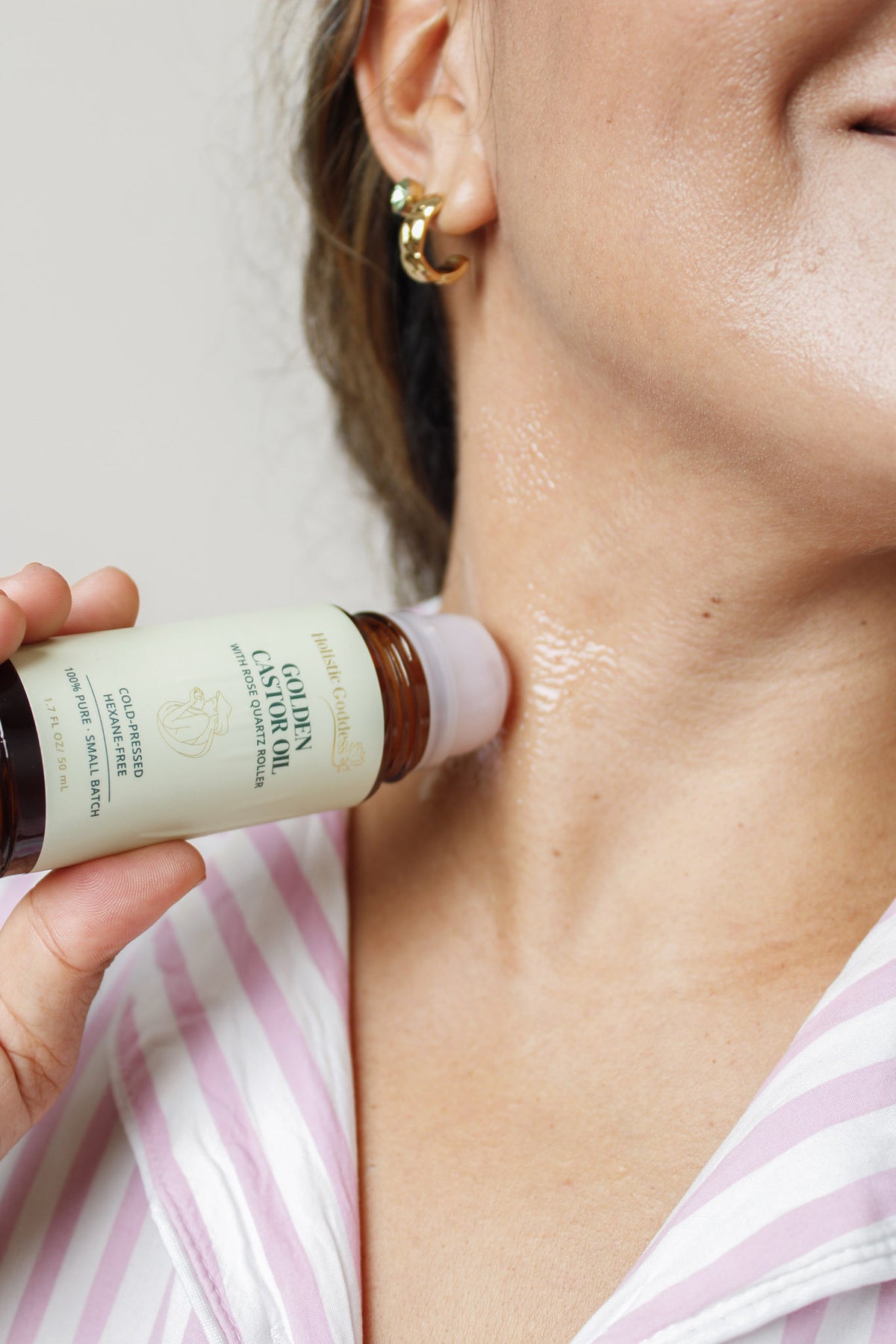 Woman applying Holistic Goddess Golden Castor Oil with a rose quartz roller to her neck