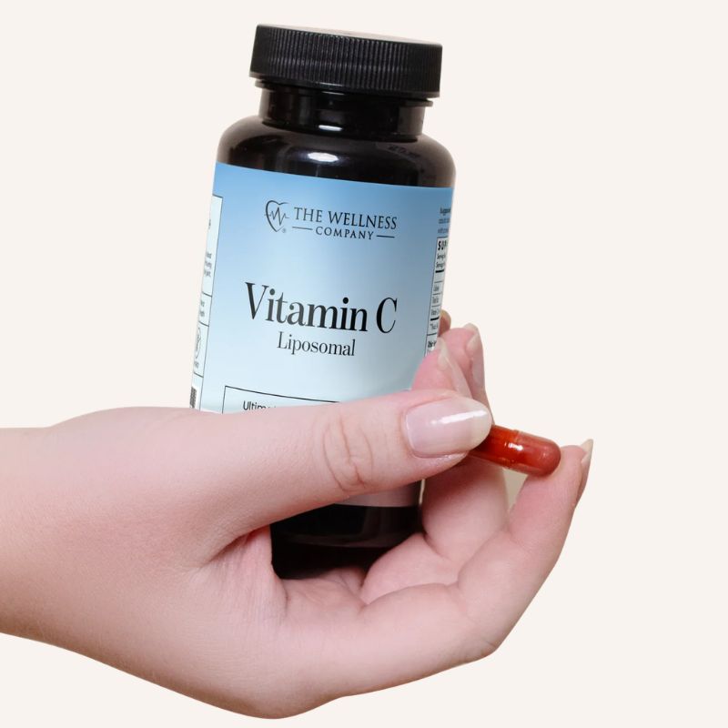 Liposomal Vitamin C by The Wellness Company – hand holding capsule beside bottle, close-up lifestyle photo