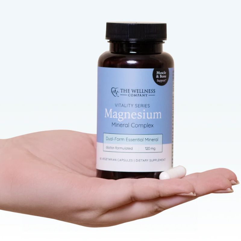 Magnesium Complex by The Wellness Company – hand holding bottle with capsule, palm-up lifestyle shot
