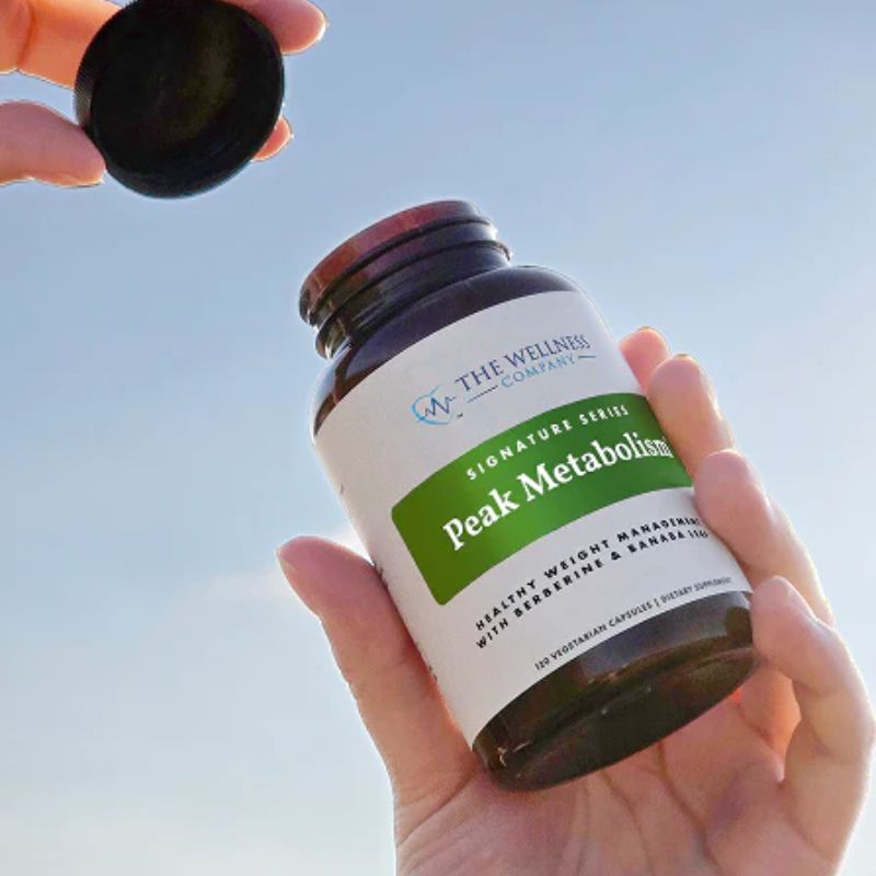 Peak Metabolism by The Wellness Company – hand holding bottle up against blue sky with cap tossed above, lifestyle photo