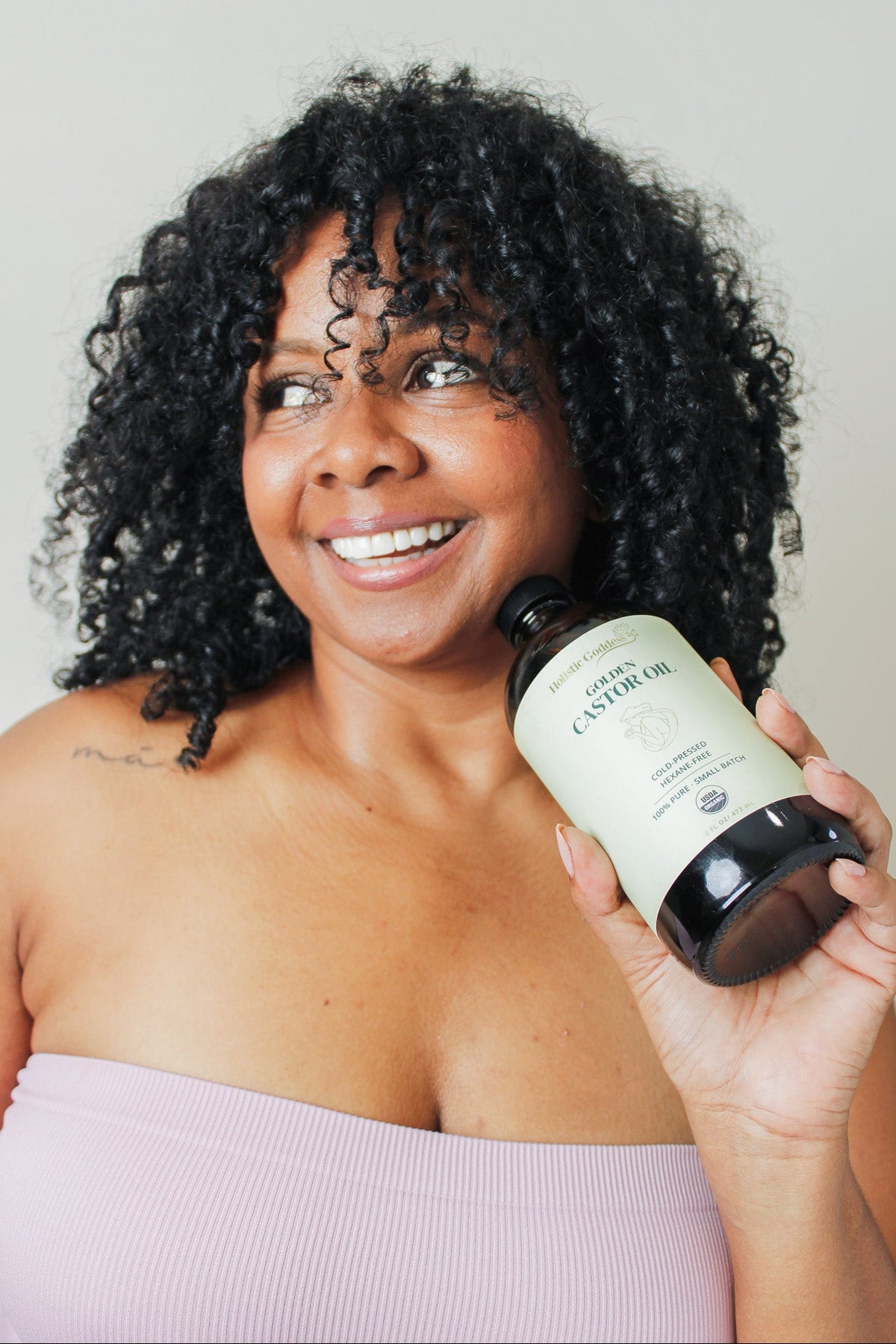 Woman holding Holistic Goddess Golden Castor Oil bottle for natural skincare